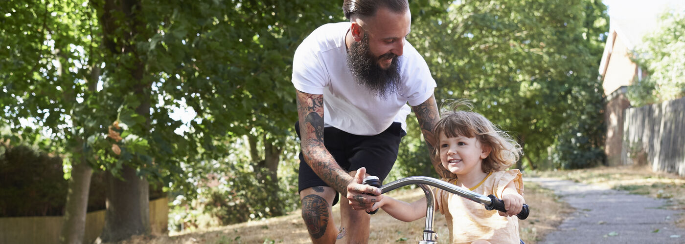 Father teaching young girl how to ride a tricycle
