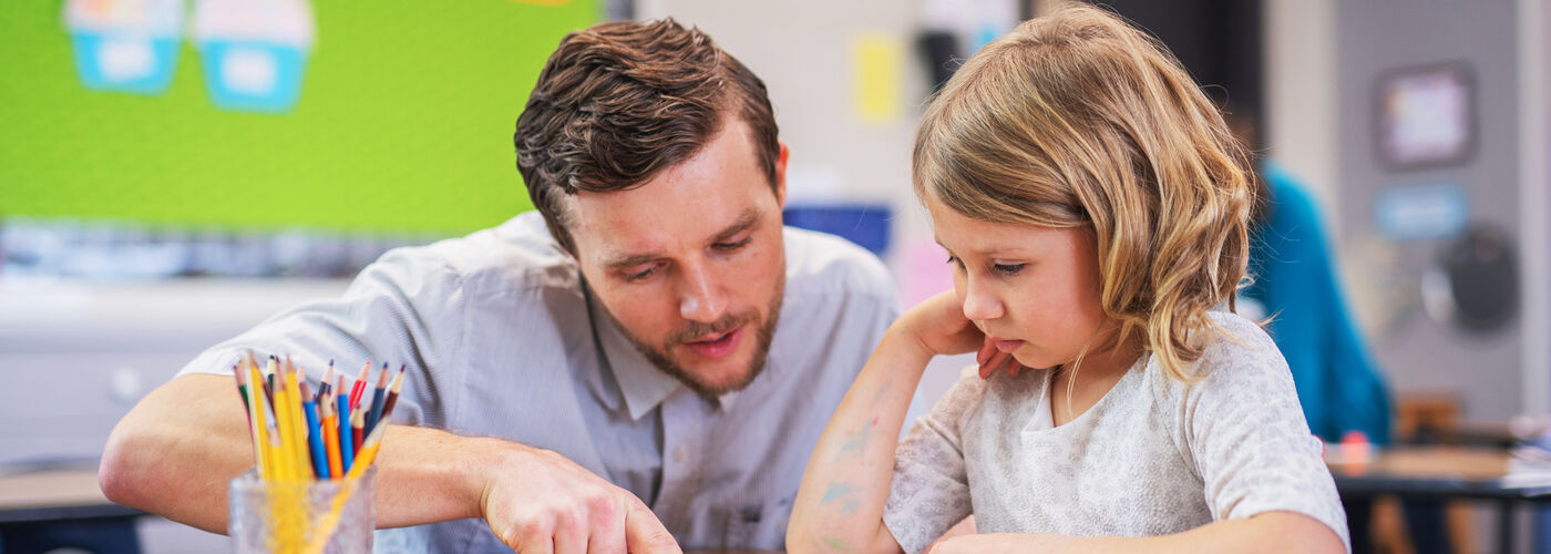 Male teacher crouched next to school girl 