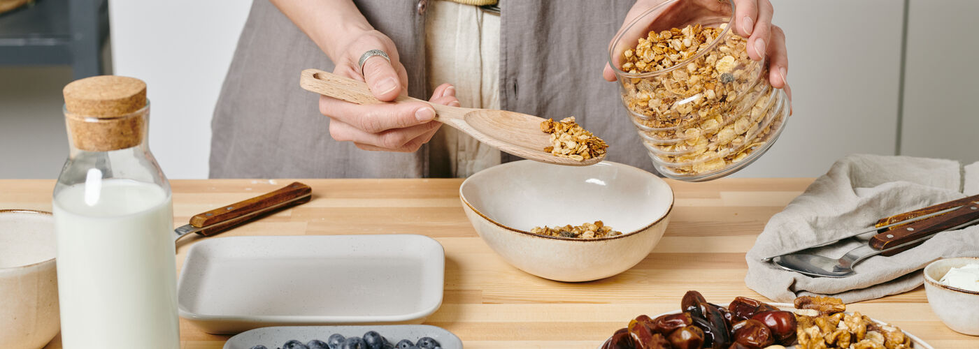 Hands of person preparing granola bowl by kitchen table