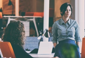 Woman sitting on desk in open plan office looking worried Woman sitting on desk in open plan office looking worried