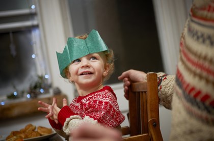 toddler enjoying christmas dinner, wearing a paper crown