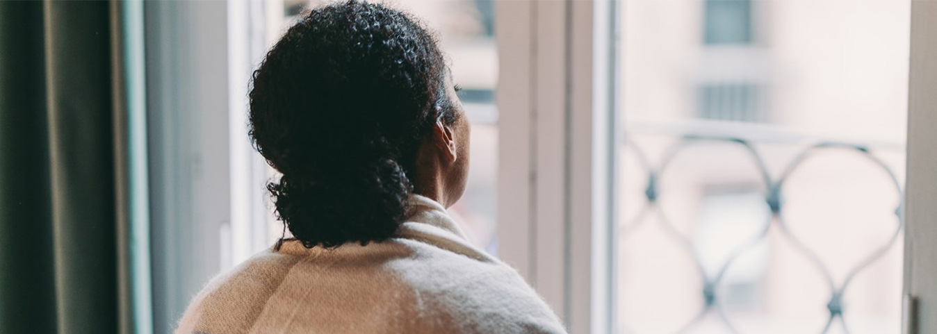 Woman looking out of her window, feeling lonely