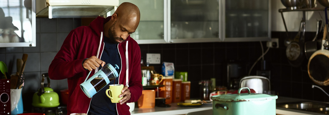 Tired male employee working from home makes coffee 