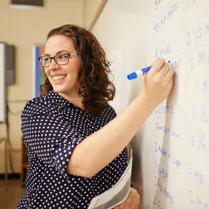 A teacher at the whiteboard, smiling at the class