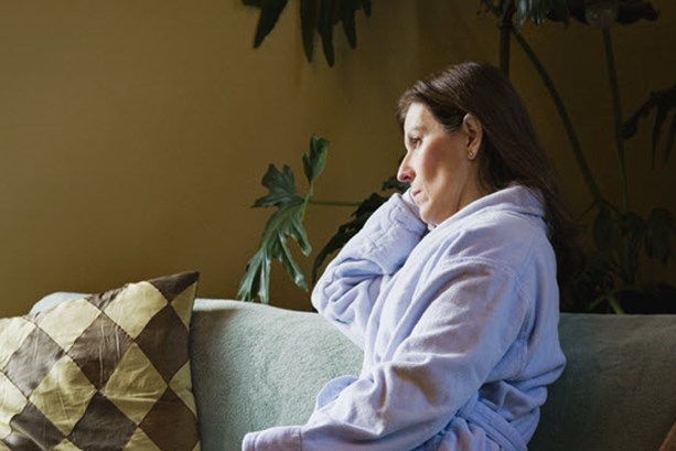 A middle-aged woman with short brown hair sat on the sofa holding a remote, looking concerned. 