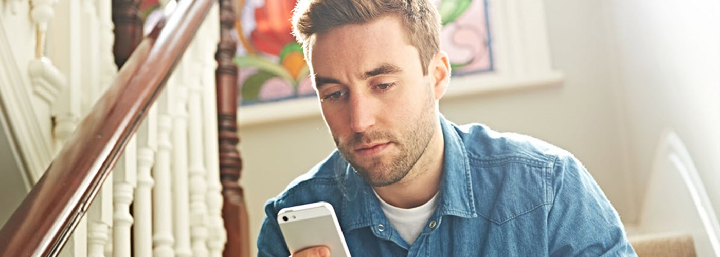 Young male with short brown hair sat on the stairs looking at his smartphone 