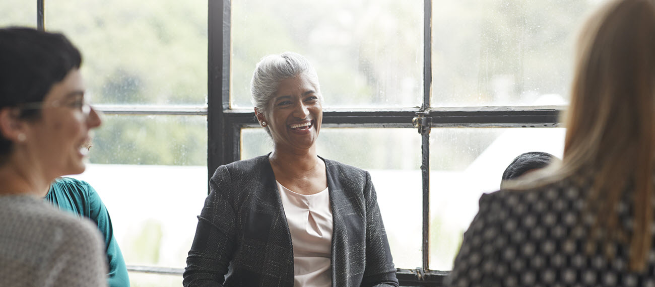 Middle aged lady in work attire smiling with two female employees 