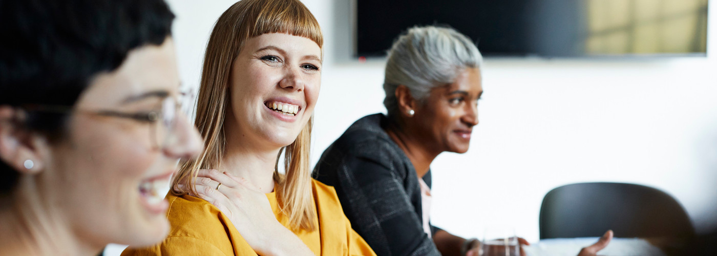 Three colleagues sitting in a meeting. They're smiling and looking positive - they support each other to tackle stress.