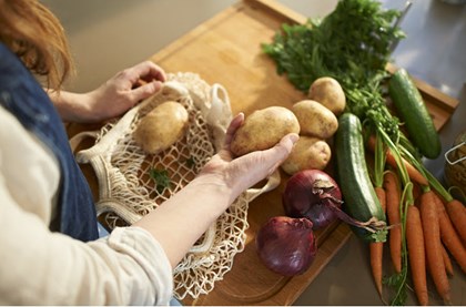 A woman looking down at a wooden chopping board containing potatoes, carrots and courgette. 