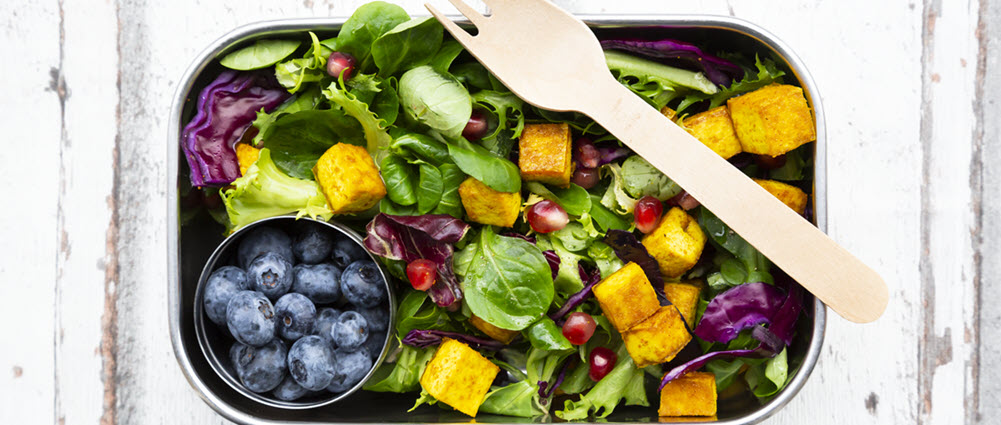 A silver rectangular bowl containing bright blue blueberries, salad, sweet potato 