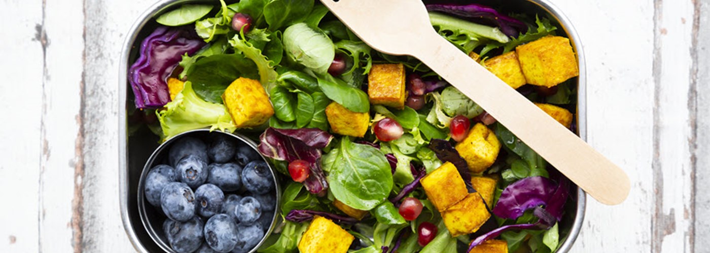 A silver rectangular bowl containing bright blue blueberries, salad, sweet potato 