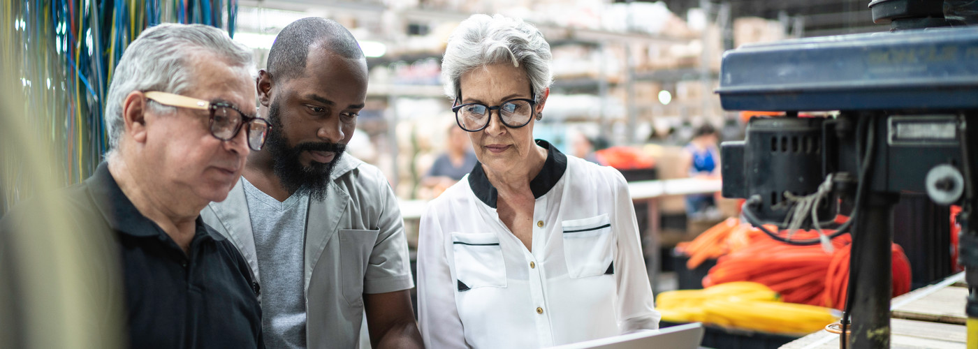 Three employees in protective eyewear, looking at a laptop within a warehouse type setting 