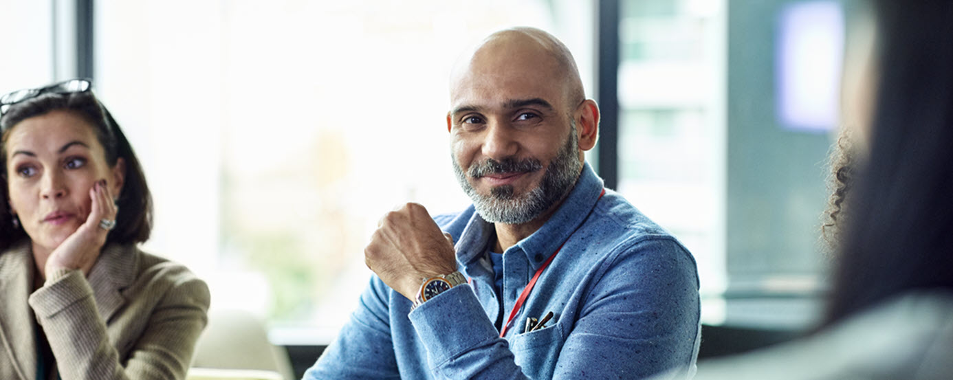 A female and male colleague sat in front of a large window, at a table, having a meeting - listening and smiling 