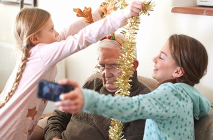 two granddaughters are putting tinsel around their dozing granddad for some Christmas day fun