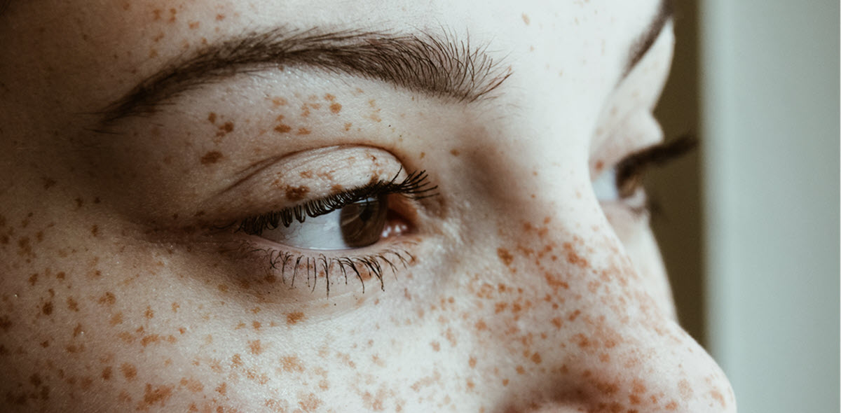 A young woman with freckles and brown eyes staring out a window 