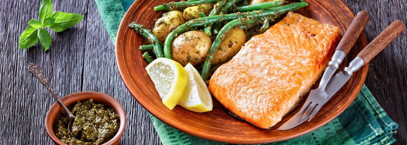 Delicious salmon dish served with green beans and potatoes on a red plate, with a side dish of pesto 