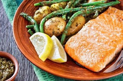 Delicious salmon dish served with green beans and potatoes on a red plate, with a side dish of pesto 