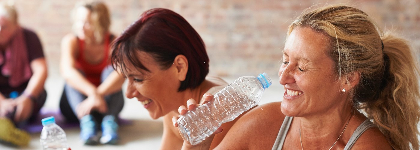 Women sat down during an exercise class, laughing and drinking a bottle of water 