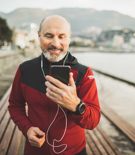 A middle aged man on a beach front pier, looking at his mobile phone 