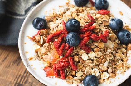 A bowl of granola, yoghurt, strawberries and blueberries on a wooden table. 