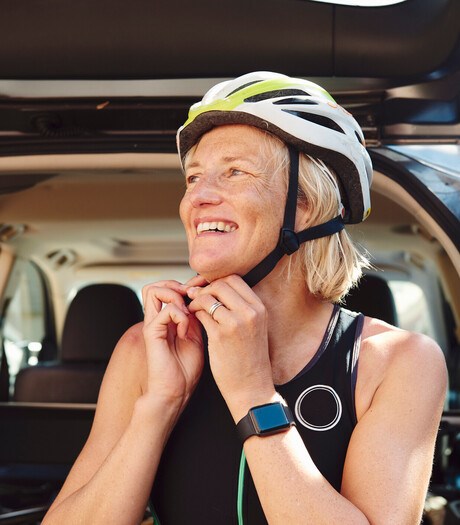 A woman fastening her helmet on whilst smiling, and wearing a smart watch on her wrist 