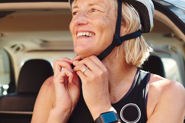 A woman fastening her helmet on whilst smiling, and wearing a smart watch on her wrist 
