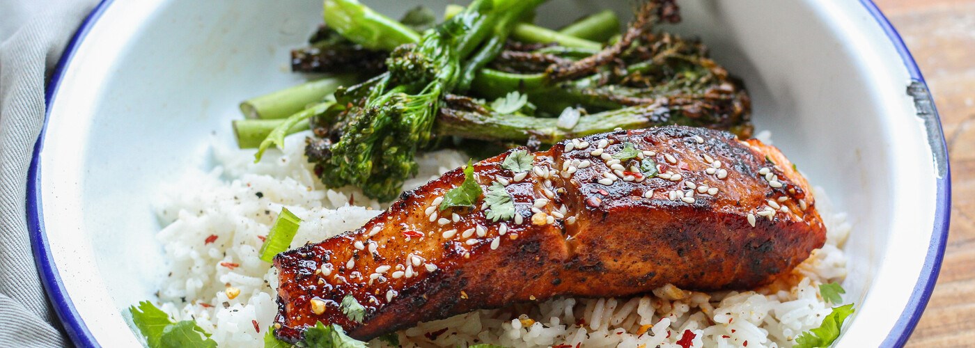 Vibrant orange salmon in a white dish, served on a bed of rice and with tender stem broccoli 