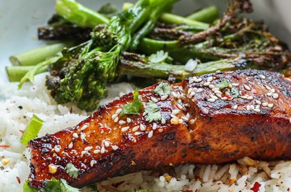 Vibrant orange salmon in a white dish, served on a bed of rice and with tender stem broccoli 