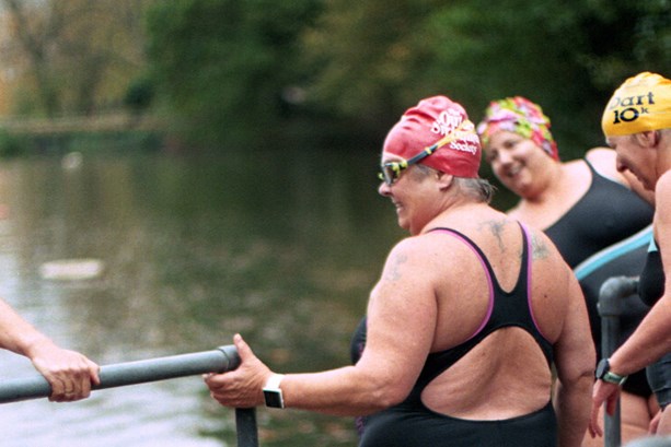 A group of middle-aged women in swimming costumes, stood next to a lake 