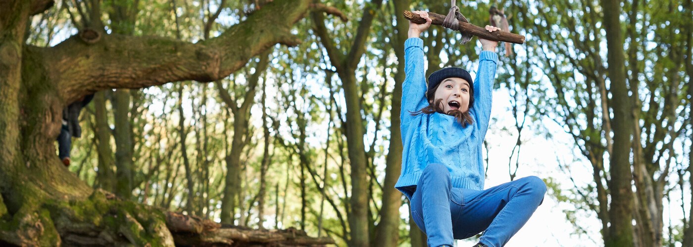 A young child swinging on a rope in a woodland. Their arms and legs are covered up to avoid tick bites.