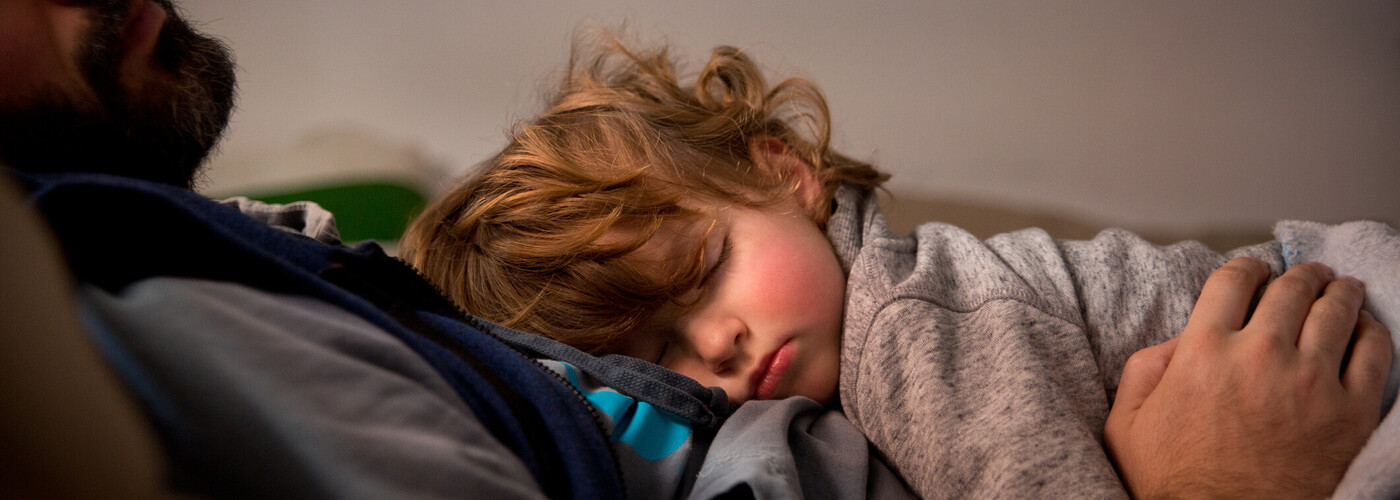 A toddler sleeping on their parent. 