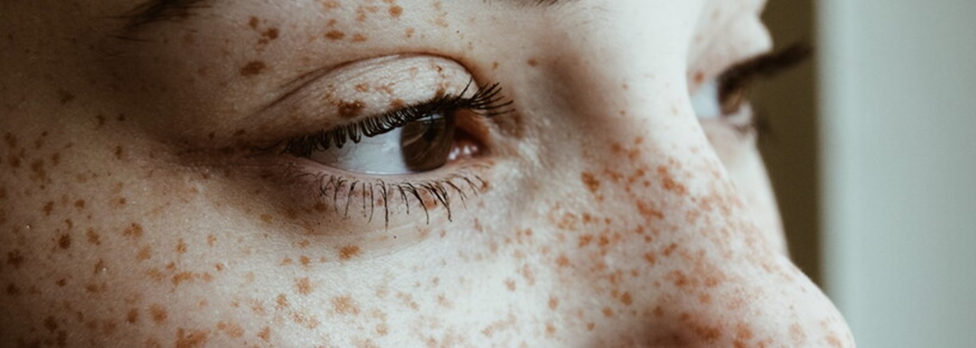 A close up of a young brown-eyed woman with freckles looking into the distance