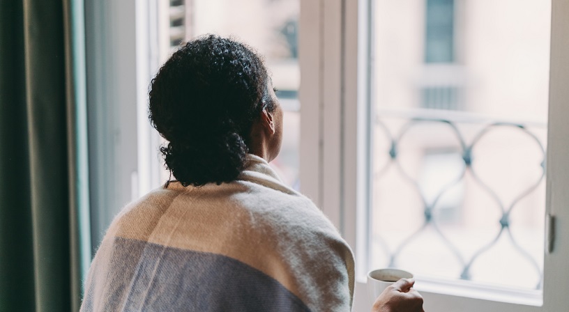 Young woman holding a coffee mug while looking through the window