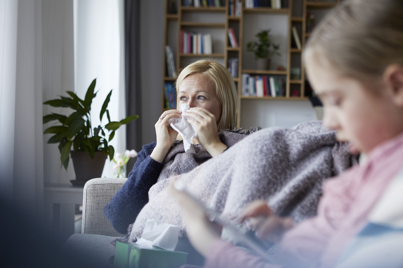 Woman with cold, flu or COVID symptoms on a sofa using a paper tissue
