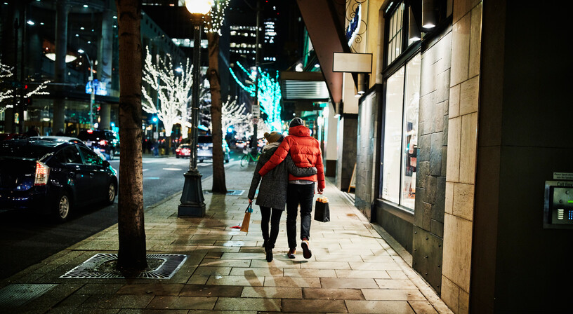 A couple taking an evening walk on a shop-lit street in winter