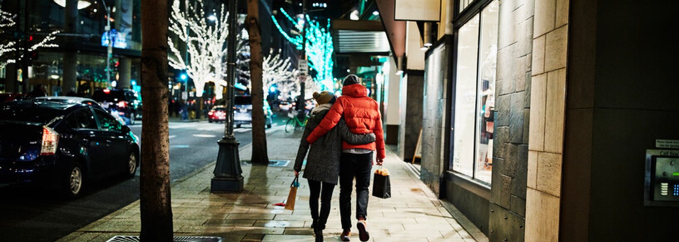 A couple taking an evening walk on a shop-lit street in winter