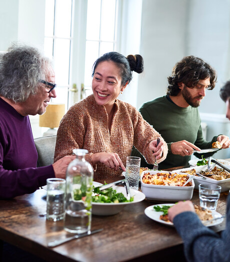Group of mixed aged relatives sitting at dining table enjoying home cooked meal