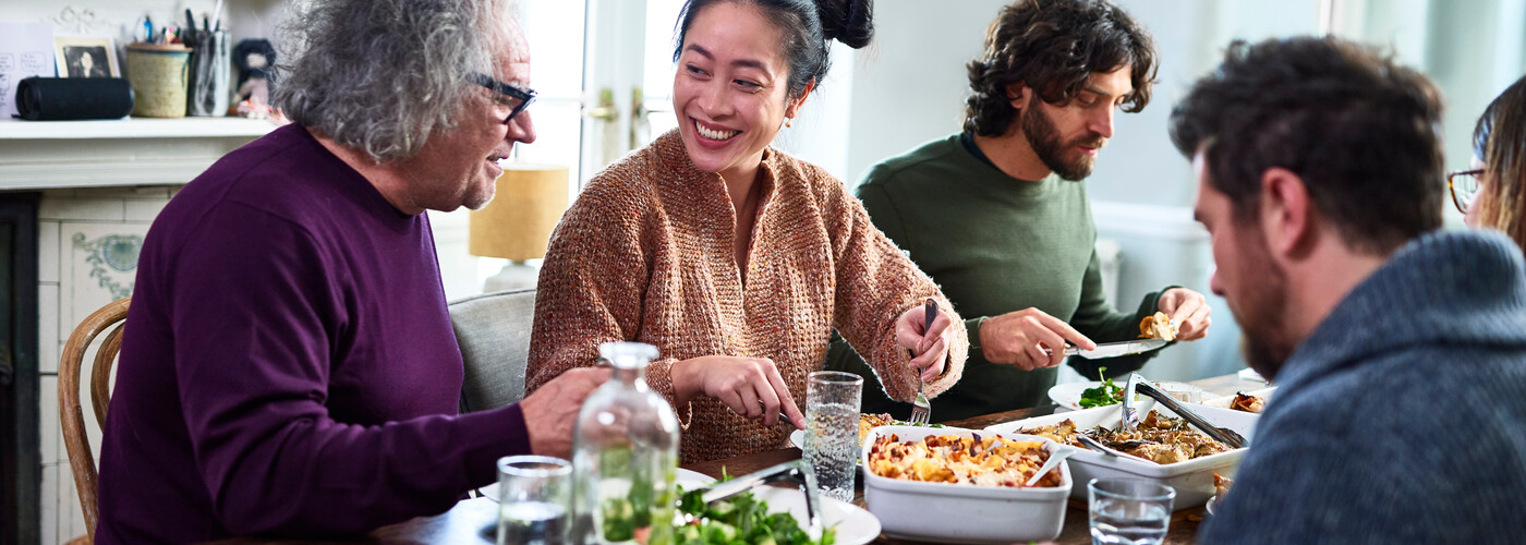 Group of mixed aged relatives sitting at dining table enjoying home cooked meal