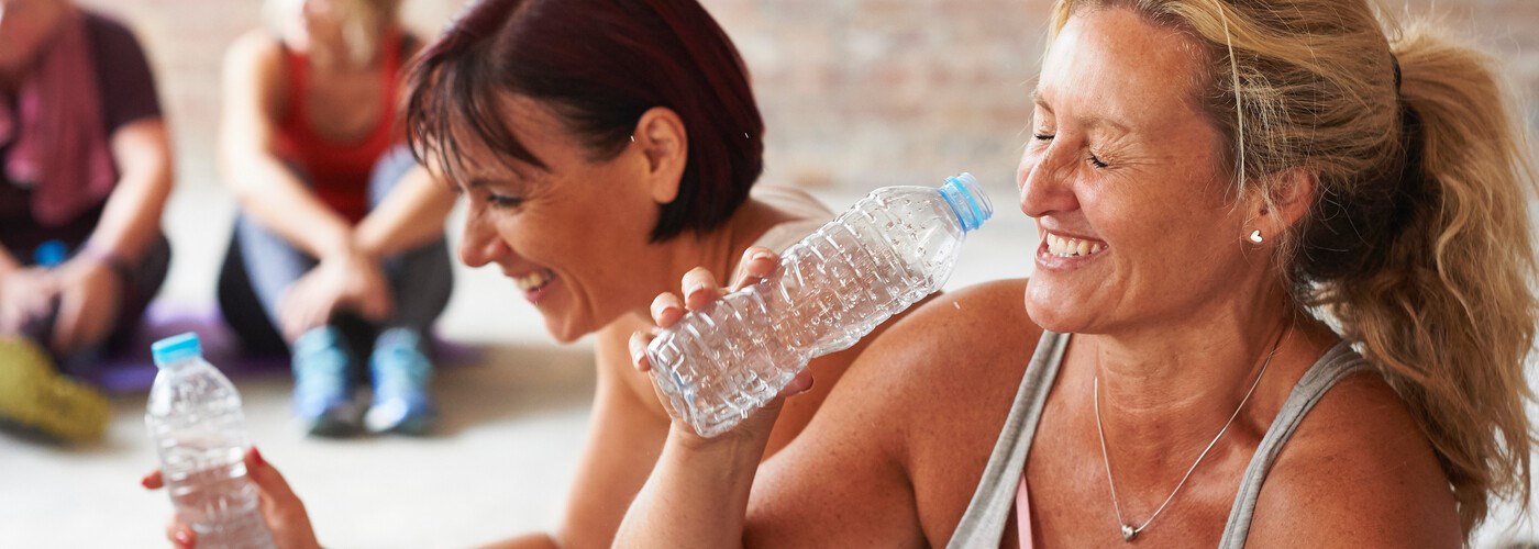 Two ladies drinking water, smiling at the gym 