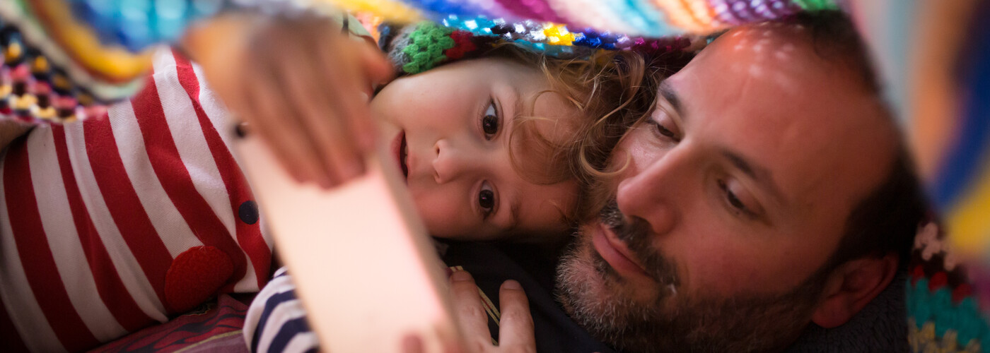 Father and son getting ready for a nap, browsing on a mobile 