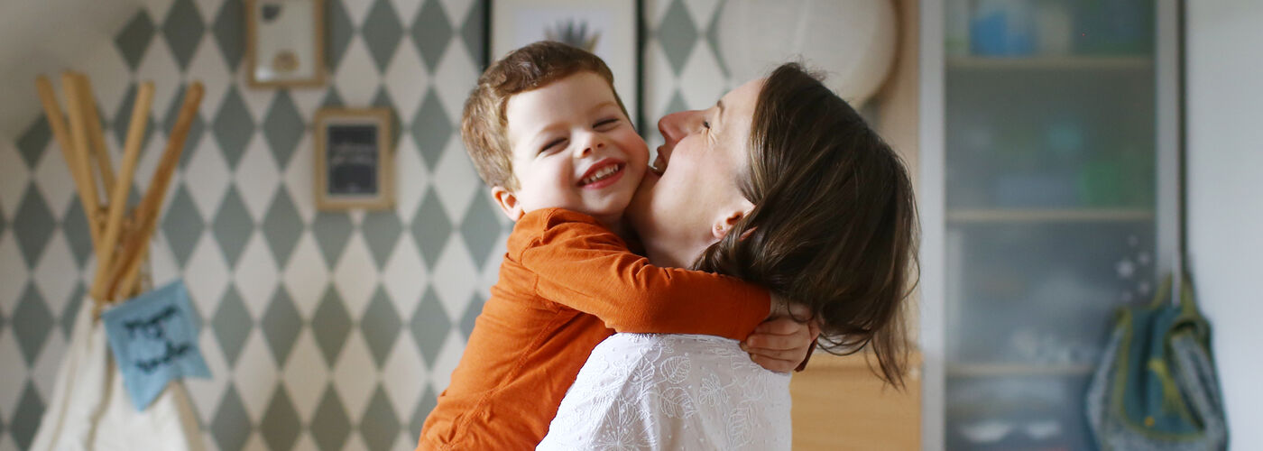 Mother and young boy embracing, laughing in child's bedroom