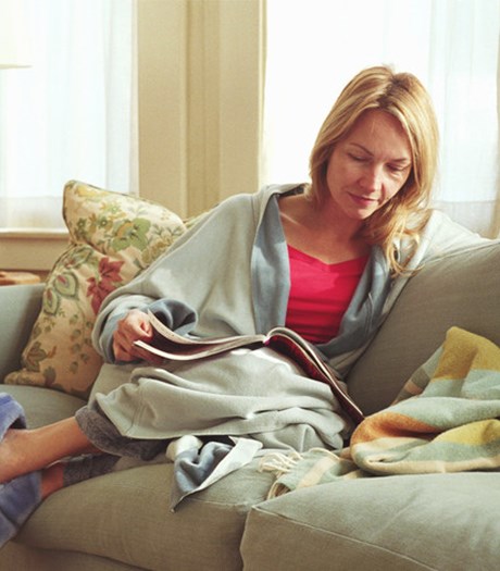 Woman with short blonde hair on the sofa with a mug and magazine, resting on a pillow 