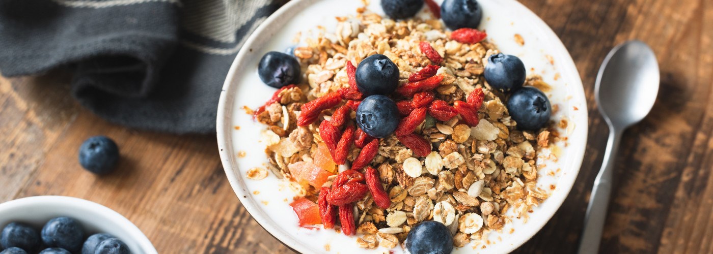 A bowl of granola, yoghurt, strawberries and blueberries on a wooden table. 